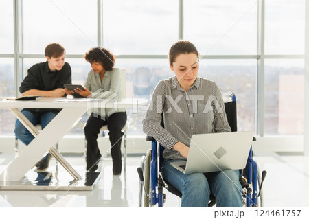 Accessible environment. Woman in chair for people with disability working with laptop in modern office. Diverse multiracial group of people colleagues working together. Young professional team Accessible environment. Woman in chair for people with disability working with laptop in modern office. Diverse multiracial group of people colleagues working together. Young professional team 124461757