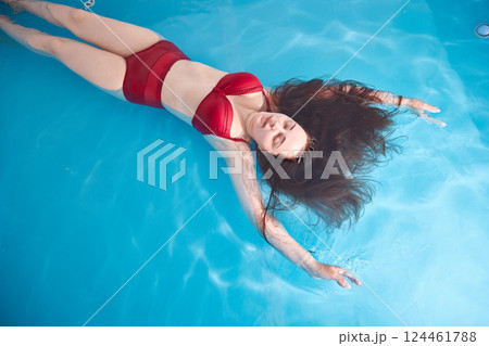 A young woman enjoys relaxing in a swimming pool or a bath with salt water. A brunette with loose hair is relaxing in a spa salon. Top view. Copy space. 124461788