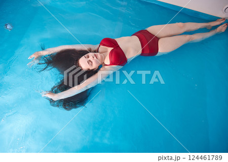 A young woman enjoys relaxing in a swimming pool or a bath with salt water. A brunette with loose hair is relaxing in a spa salon. Top view. Copy space. 124461789