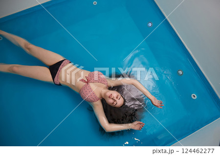 Top view of an attractive young woman floating on blue water. Relaxation and spa therapy. Top view. Copy Space 124462277
