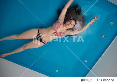A young girl enjoys relaxing in a pool with concentrated sea water. Floating. Top view. Copy space 124462278
