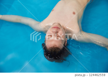 Man is swimming in the pool on his back with his arms spread wide. Wellness, relaxation and spa therapy. Copy space. 124462559