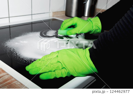 A man wearing cleaning gloves wipes the induction hob. 124462977