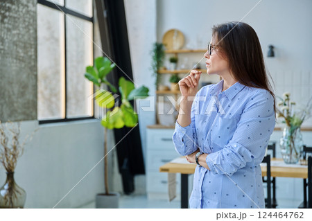 Portrait of serious middle aged woman looking out window in home Portrait of serious middle aged woman looking out window in home 124464762