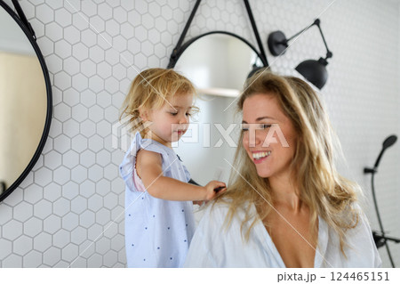 Cute little girl brushing, combing mother's long hair. Cute little girl brushing, combing mother's long hair. 124465151