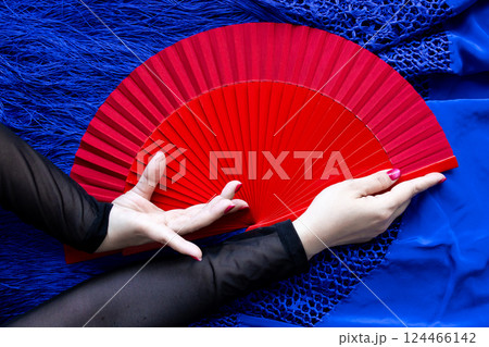Elegant hand holding red fan on blue fabric background 124466142