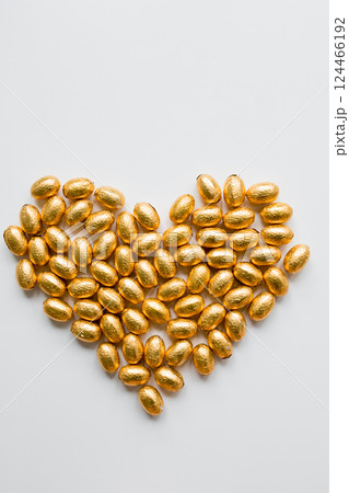 Golden foil wrapped chocolate eggs arranged in heart shape on white background 124466192