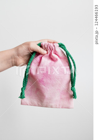 Hand holding pink drawstring bag with green rope against white background Hand holding pink drawstring bag with green rope against white background 124466193