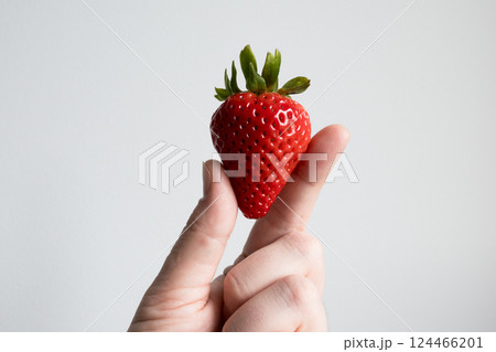 Hand holding ripe red strawberry against light background 124466201