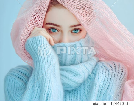 Fashionable woman with curly hair wearing a stylish pink sweater poses against a blue wall with window shadows 124470133