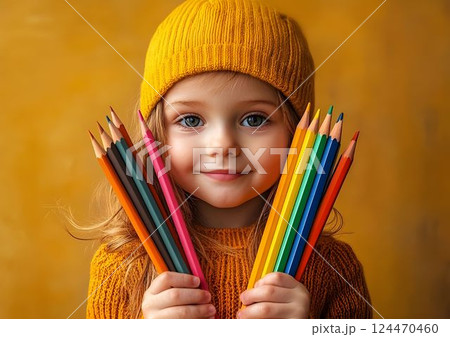 Young child gripping colorful pencils near face, blue eyes peeking over drawing tools, showcasing childhood curiosity and artistic imagination 124470460