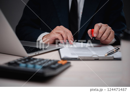 person stamping documents with a rubber stamp at a desk, representing business approval, legal contracts, and paperwork processing in an office environment. person stamping documents with a rubber stamp at a desk, representing business approval, legal contracts, and paperwork processing in an office environment. 124471487