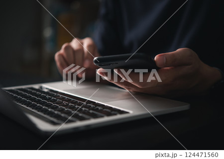 man holding a smartphone while typing on a laptop keyboard in an office or home setting, representing online work, business tasks, emails, and internet communication using technology. man holding a smartphone while typing on a laptop keyboard in an office or home setting, representing online work, business tasks, emails, and internet communication using technology. 124471560