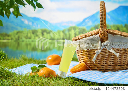 Unlabeled tube of yellow liquid cream, leaning diagonally against a hand-woven wicker basket. Citrus with vibrant hues placed around on a fabric rug. Natural setting, concept of a picnic in the park. Unlabeled tube of yellow liquid cream, leaning diagonally against a hand-woven wicker basket. Citrus with vibrant hues placed around on a fabric rug. Natural setting, concept of a picnic in the park. 124472298
