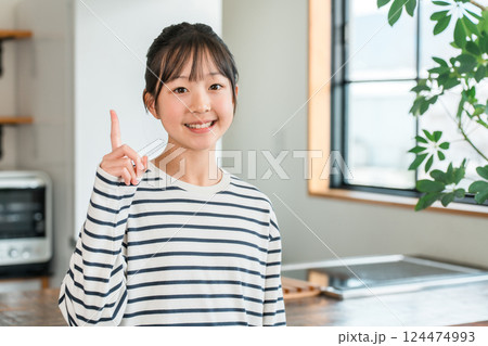 家のキッチン・ダイニングで指差しサインする小学生・中学生の女の子（ボーダー・カジュアル） 124474993