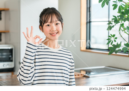 家のキッチン・ダイニングでOKサインする小学生・中学生の女の子（ボーダー・カジュアル） 124474994