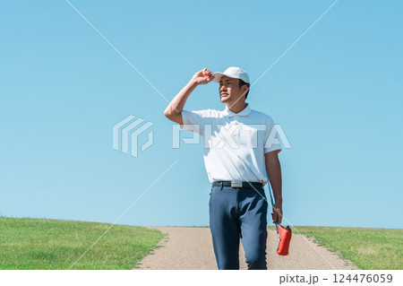 パターとゴルフクラブを持ってゴルフ場を歩く男性 パターとゴルフクラブを持ってゴルフ場を歩く男性 124476059