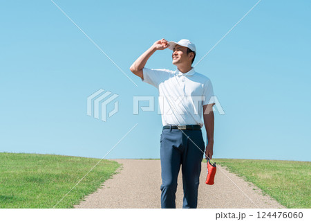 パターとゴルフクラブを持ってゴルフ場を歩く男性 124476060