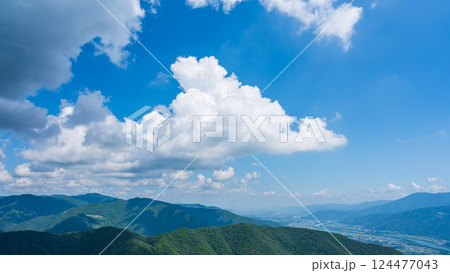 青空に流れるたくさんの白い雲と、緑に包まれた山々 124477043