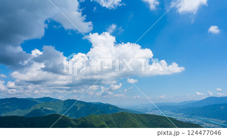 青空に流れるたくさんの白い雲と、緑に包まれた山々 124477046