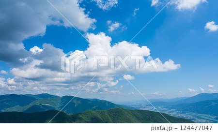 青空に流れるたくさんの白い雲と、緑に包まれた山々 124477047