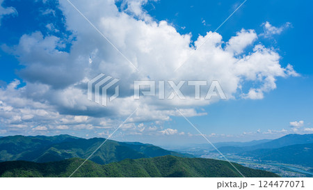 青空に流れるたくさんの白い雲と、緑に包まれた山々 124477071