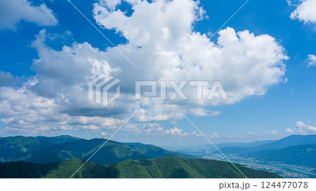 青空に流れるたくさんの白い雲と、緑に包まれた山々 124477078
