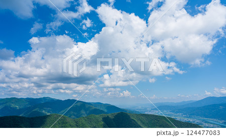 青空に流れるたくさんの白い雲と、緑に包まれた山々 124477083