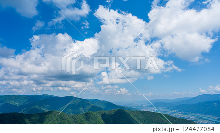 青空に流れるたくさんの白い雲と、緑に包まれた山々 124477084