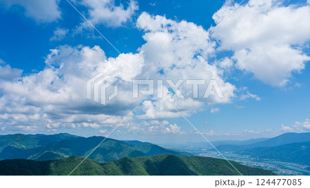 青空に流れるたくさんの白い雲と、緑に包まれた山々 124477085