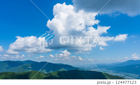 青空に流れるたくさんの白い雲と、緑に包まれた山々 124477123