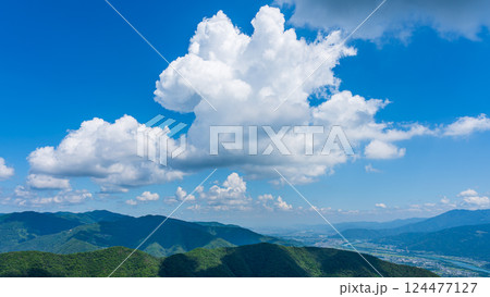 青空に流れるたくさんの白い雲と、緑に包まれた山々 124477127