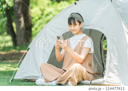 キャンプ場でテントの前でスマホを見ている女の子 124477611