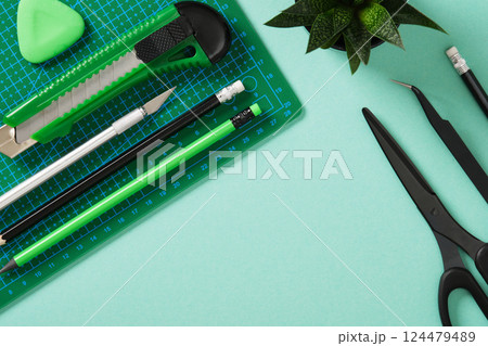 Paper crafts work table flatlay. Tools for hobby, green cutting mat, scissors, tweezers, craft knife, pencil, eraser on a mint green background. Space for your text. Paper crafts work table flatlay. Tools for hobby, green cutting mat, scissors, tweezers, craft knife, pencil, eraser on a mint green background. Space for your text. 124479489