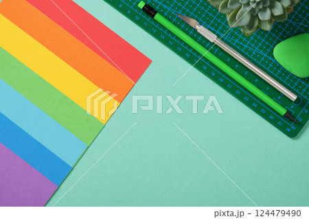 Paper crafts art table flatlay. Tools for hobby, green cutting mat, craft knife, pencil, eraser, colored paper on turquoise background. Space for your text. Paper crafts art table flatlay. Tools for hobby, green cutting mat, craft knife, pencil, eraser, colored paper on turquoise background. Space for your text. 124479490