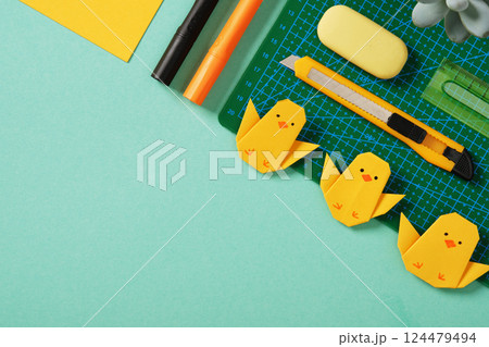 Frame made of paper crafting tools: office knife, ruler, eraser and yellow paper on mint green background. Yellow origami chickens. DIY concept, copyspace 124479494