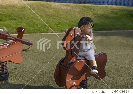 A Toddler Sits On A Rocking Horse In The Garden A Toddler Sits On A Rocking Horse In The Garden 124480498