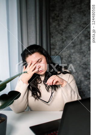 Woman working from home office sitting with laptop rubbing tired eyes. Burnout, stress, fatigue at work concept 124480508