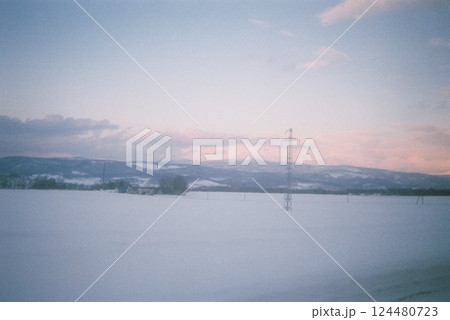 雪原に沈む夕光と遠くの山と電線塔 124480723