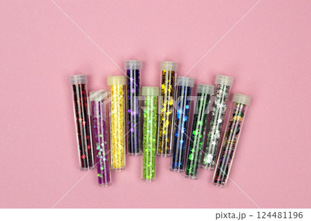 An assortment of bright, shiny sequins in small jars scattered across a pink background, catching the light perfectly. An assortment of bright, shiny sequins in small jars scattered across a pink background, catching the light perfectly. 124481196