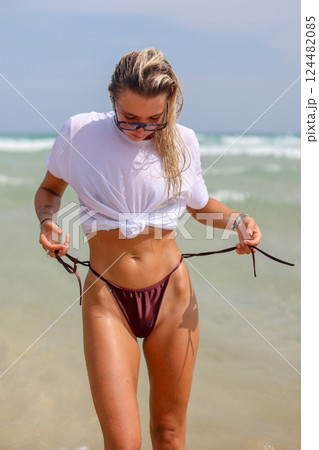 A woman dressed in a bikini and wearing sunglasses is walking along the beach A woman dressed in a bikini and wearing sunglasses is walking along the beach 124482085
