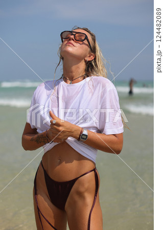 A woman in a white shirt and sunglasses is on the beach 124482089