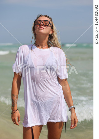 A woman in a white shirt and sunglasses is on the beach 124482092