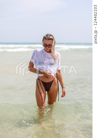 A woman is confidently walking out of the vast ocean onto the beach 124482103