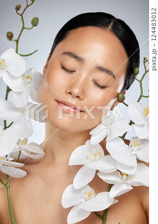 Asian woman, orchid flower and skincare on studio background in relax wellness, health and face. Portrait of smile and happy model in self care makeup with plant for soft and perfect skincare beauty 124483012