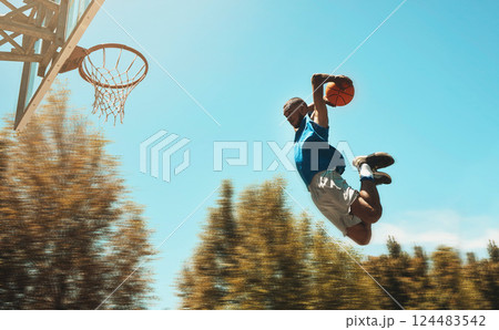 Basketball, sports and dunk with a man athlete jumping or flying through the air to score while playing on an outdoor court against the sky. Sport, fitness and exercise with a male basketball player 124483542