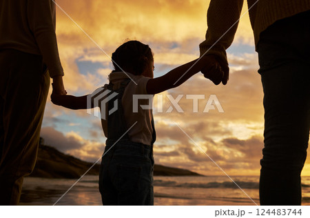 Parents, child and silhouette of holding hands on the beach during sunset for family bonding in the outdoors. Kid hand, mother and father enjoying the scenic view, care and freedom on the ocean coast 124483744