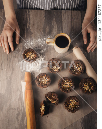 Female hands, coffee mug, freshly baked muffins on baking paper and rolling pin on a table, vertical image. Female hands, coffee mug, freshly baked muffins on baking paper and rolling pin on a table, vertical image. 124487277