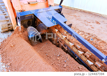 Heavy trencher machinery operates to create trench in sandy soil for construction purposes 124487394