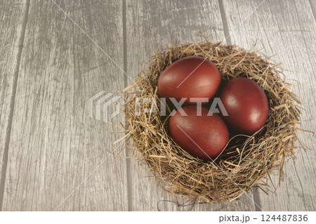 Red eggs in birds nest made from hay on wooden white background, top view, copy space. Atmospheric Easter concept. Red eggs in birds nest made from hay on wooden white background, top view, copy space. Atmospheric Easter concept. 124487836
